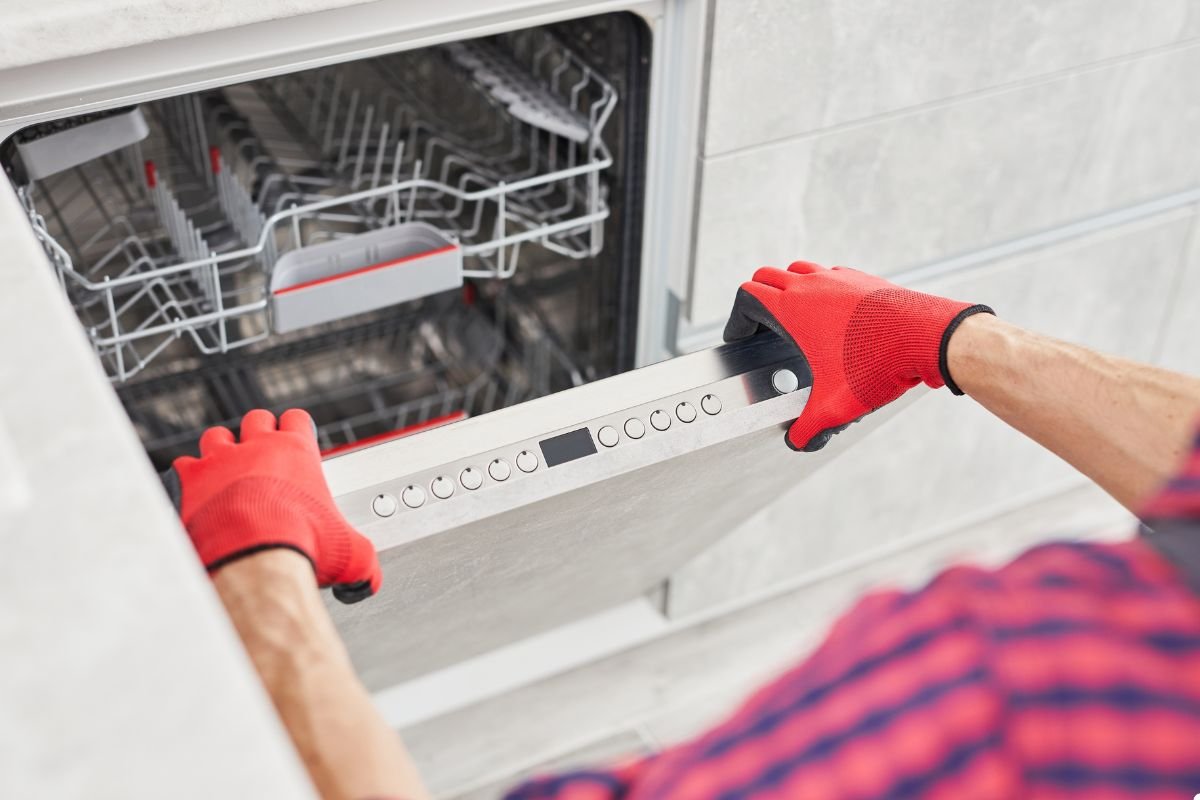 A man wearing red gloves is holding a dishwasher, preparing for installation or maintenance tasks.