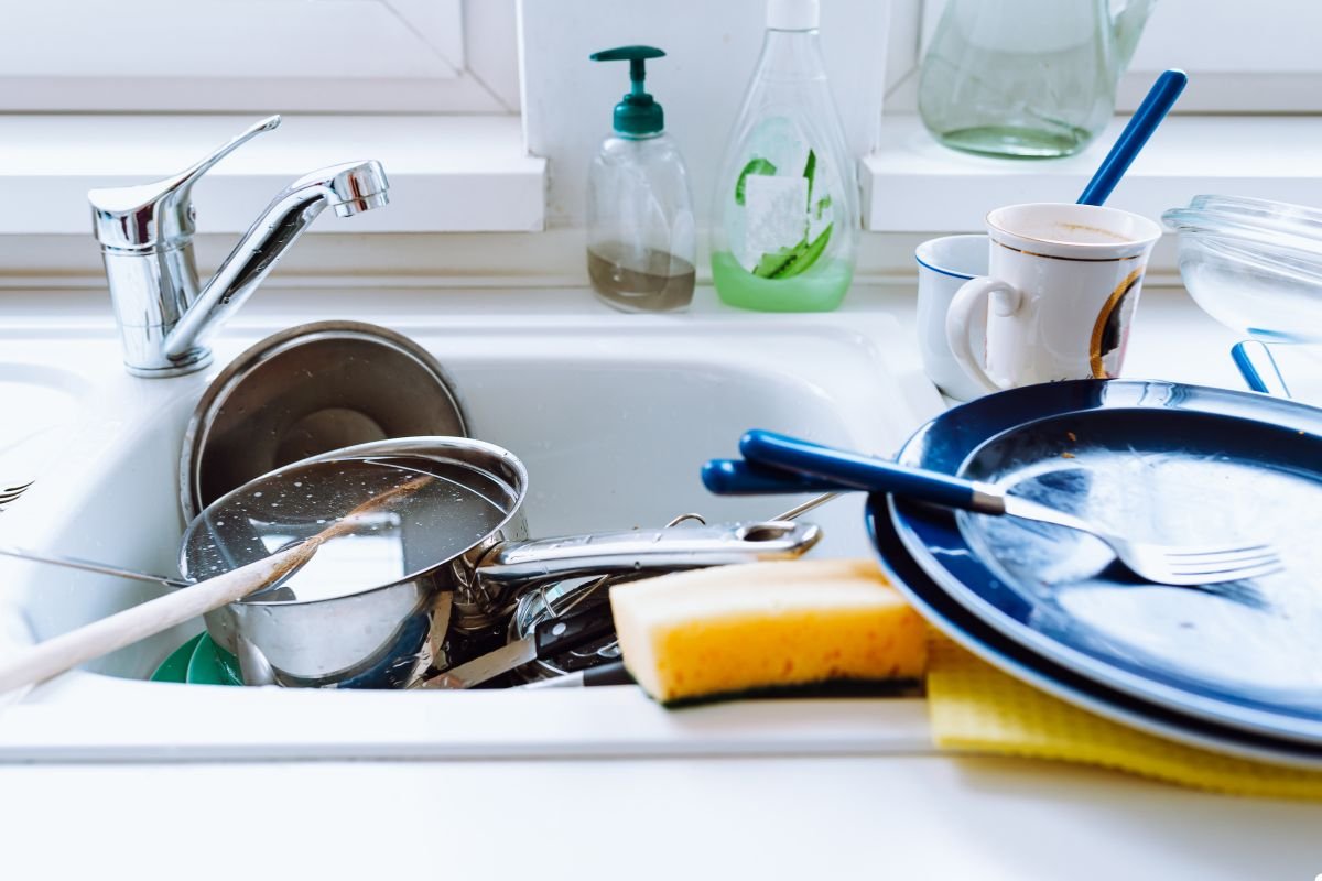 A sink containing a pile of dirty dishes and utensils, illustrating the aftermath of a meal preparation.