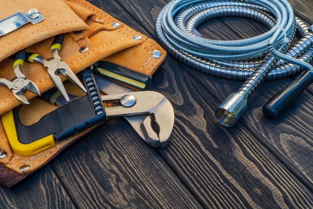 An assortment of plumbing tools and supplies arranged on a wooden table, featuring wrenches, pipes, and connectors.